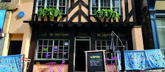 The black timber-framed exterior of Three Cranes in Rotherham, with hanging flower boxes, outdoor tables and a chalkboard sign.